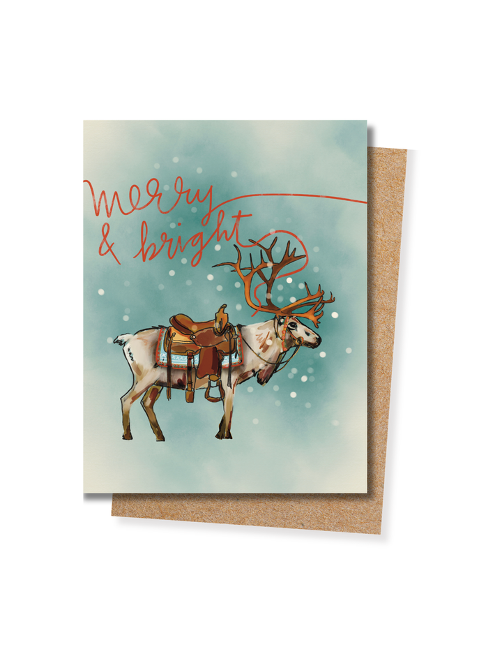 Merry & Bright Christmas card in pale blue, featuring a reindeer wearing a western saddle, with a kraft envelope
